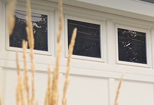 New white recessed panel double garage door with windows on a dark gray colored home