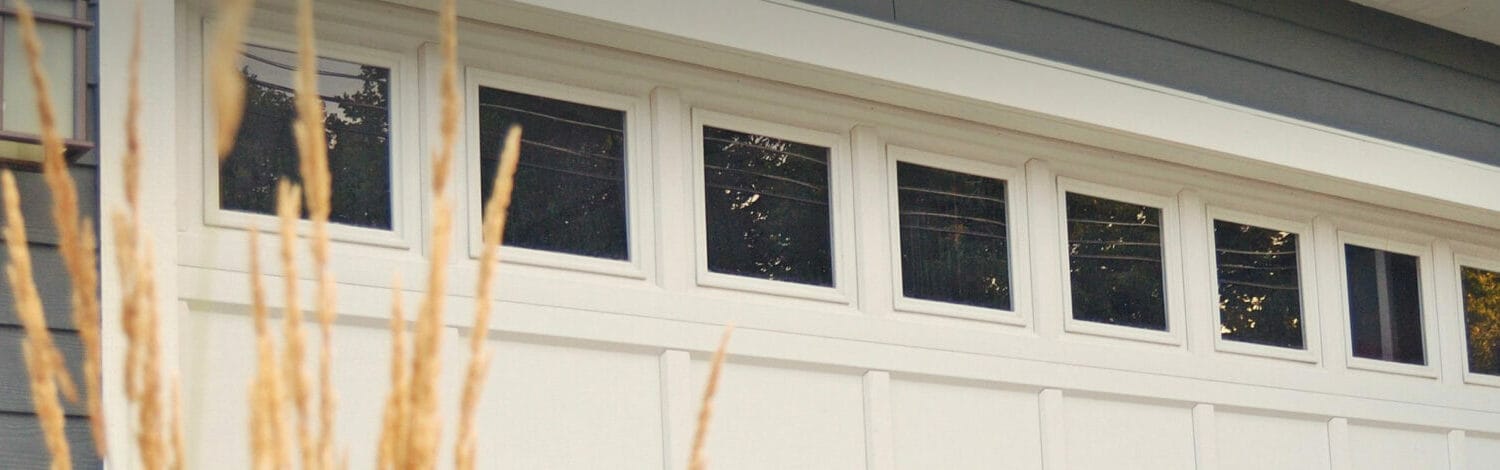 New white recessed panel double garage door with windows on a dark gray colored home
